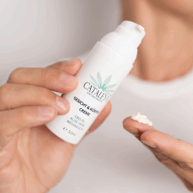 Eine Hand hält den weißen Pumpspender der CATALEYA Gesicht- und Körpercreme mit CBD-Öl, Aloe Vera und Weihrauch, während auf einer Fingerkuppe ein kleiner Tupfer Creme zu sehen ist.