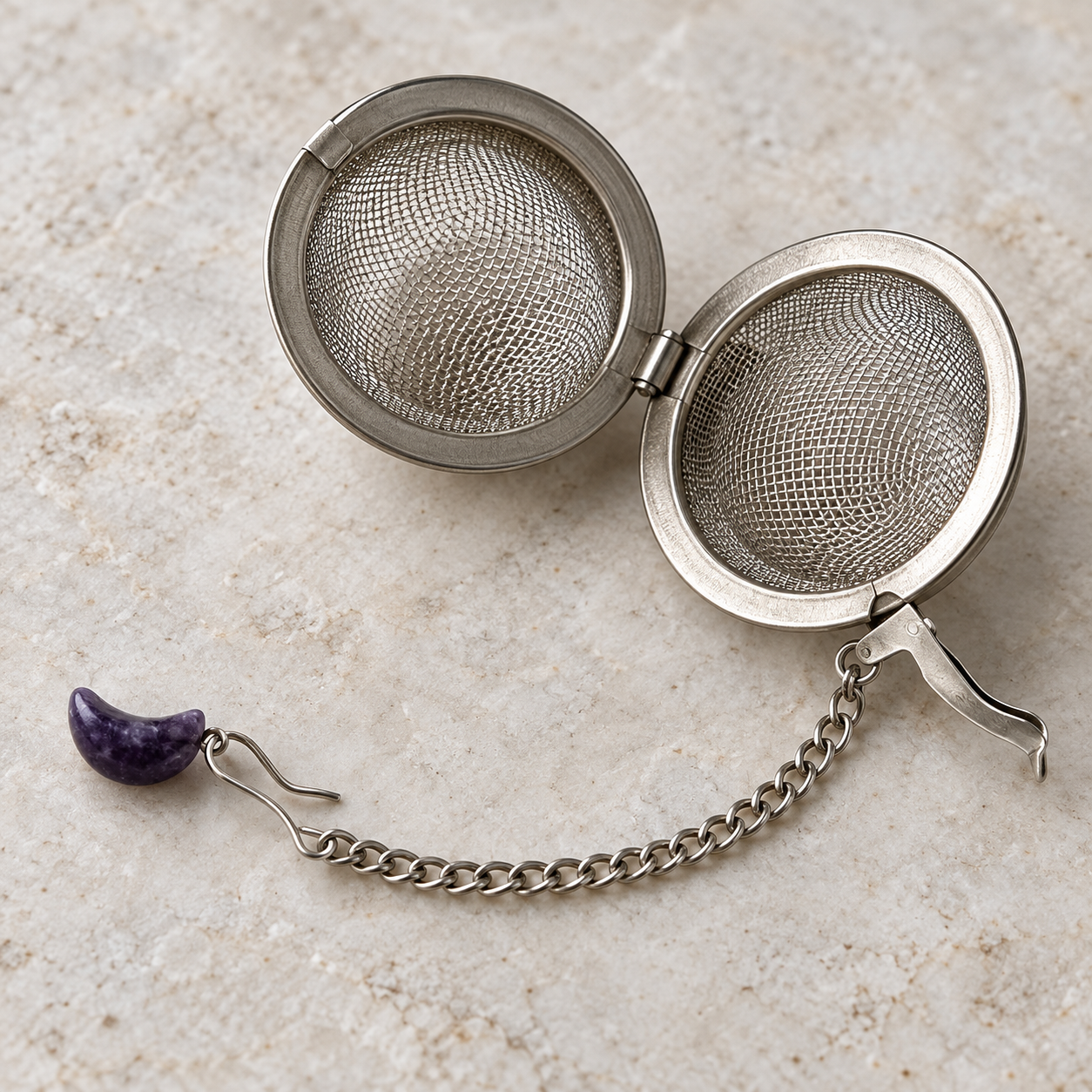 Geöffnetes rundes Mesh-Tee-Ei mit Kette, Haken und lilafarbenem Mondanhänger im Detail